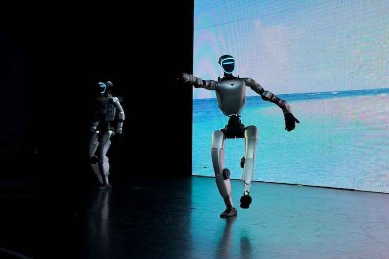 Two humanoid robots on a stage with a bright digital screen background, showing modern technology, automation, and a futuristic presentation Robot Unitree G1 energylandia Poland, Zator